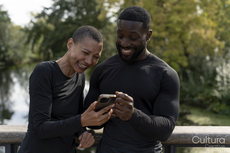 Smiling athletic man and woman looking at smart phone in park