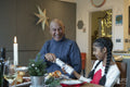 Girl with grandfather holding Christmas cracker at table