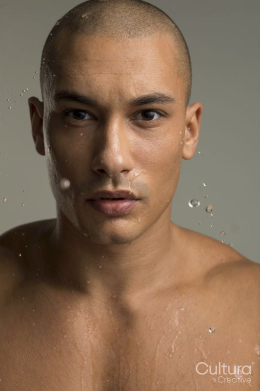 Studio portrait of shirtless man splashing water on face