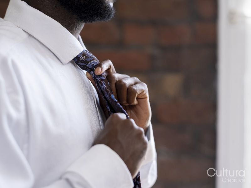 Close-up of person in white shirt tying necktie
