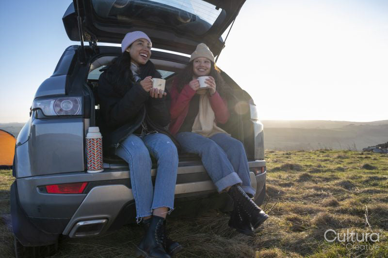 Female friends sitting in car trunk and drinking tea