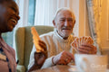 Smiling senior man and nurse playing cards at table in nursing home