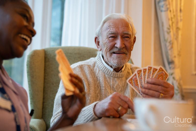 Smiling senior man and nurse playing cards at table in nursing home