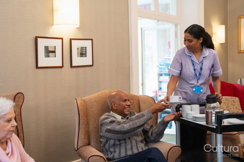 Female employee serving tea to senior man in nursing home
