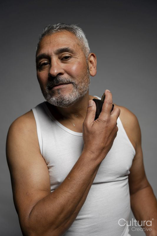 Portrait of man putting on perfume against gray background