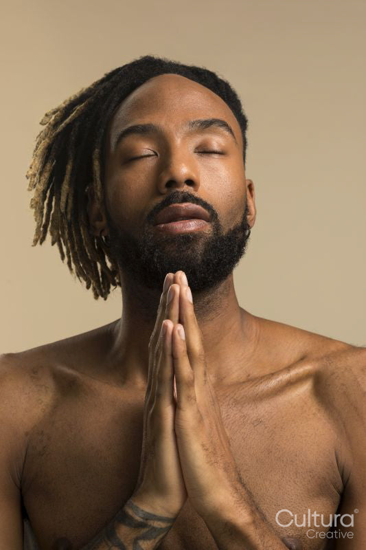 Studio shot of young man with dreadlocks praying