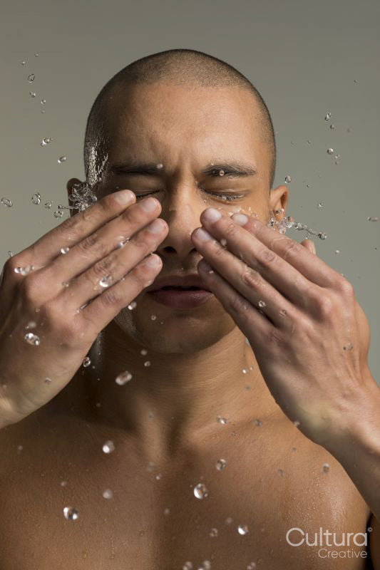 Studio shot of shirtless man splashing water on face