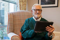 Senior man sitting in armchair and using tablet in nursing home