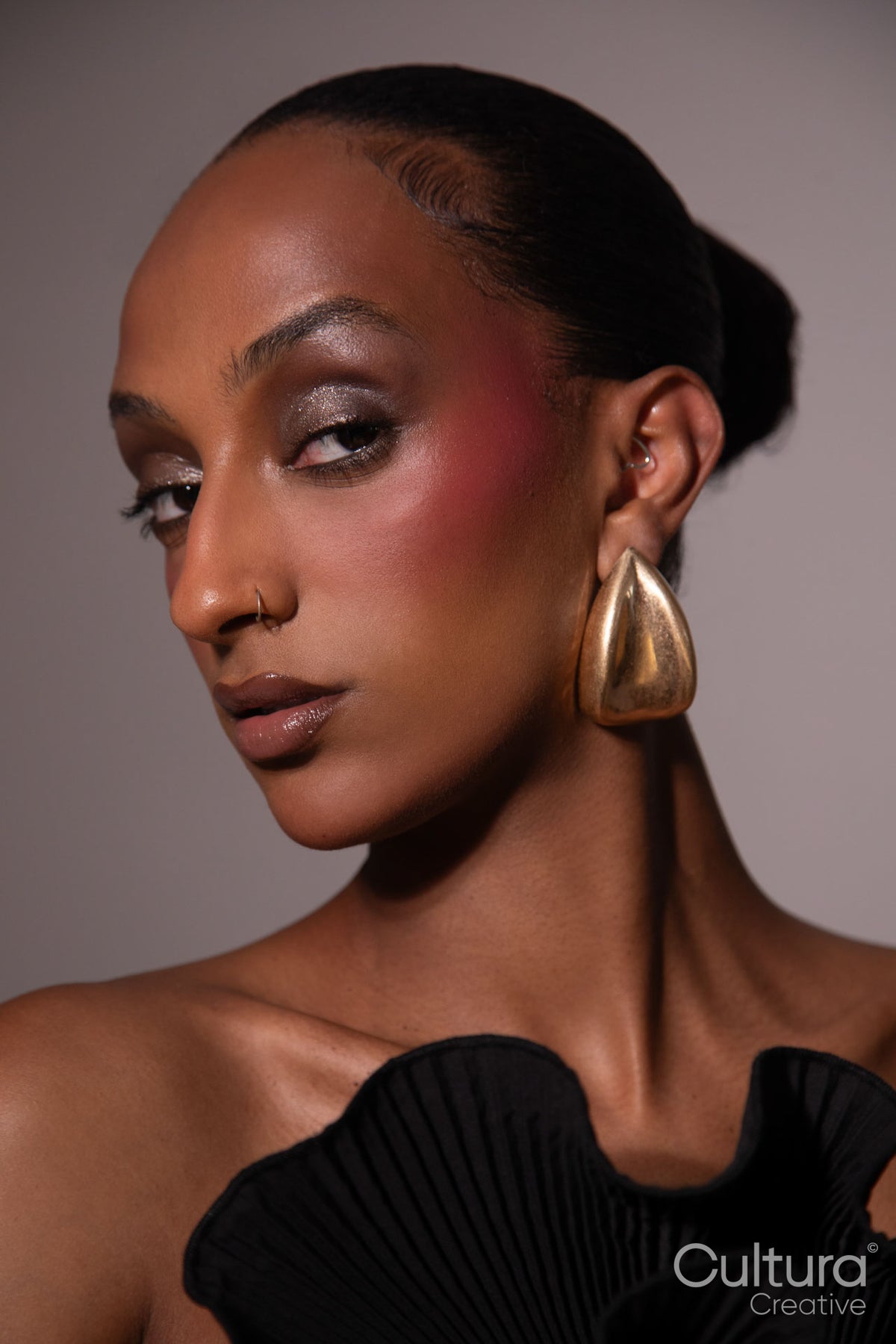 Woman in a black dress with gold earrings on a grey background