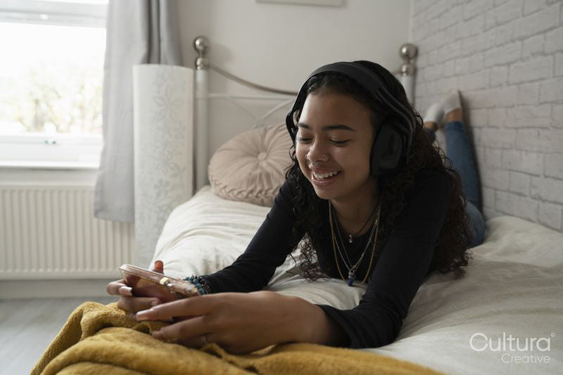 Teenage girl listening music on smart phone while lying on bed at home