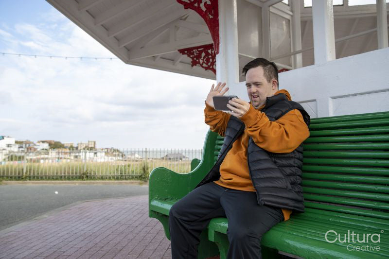 Man sitting on bench and waving to smart phone