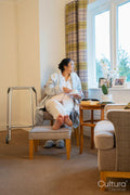Senior lady sitting with coffee and looking through window in bedroom at nursing home