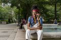 Portrait of young woman sitting on wall in park, talking on smart phone