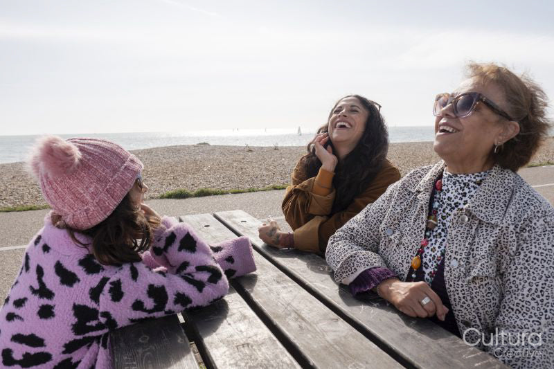 Grandmother, mother and daughter laughing while sitting by picnic table on beach
