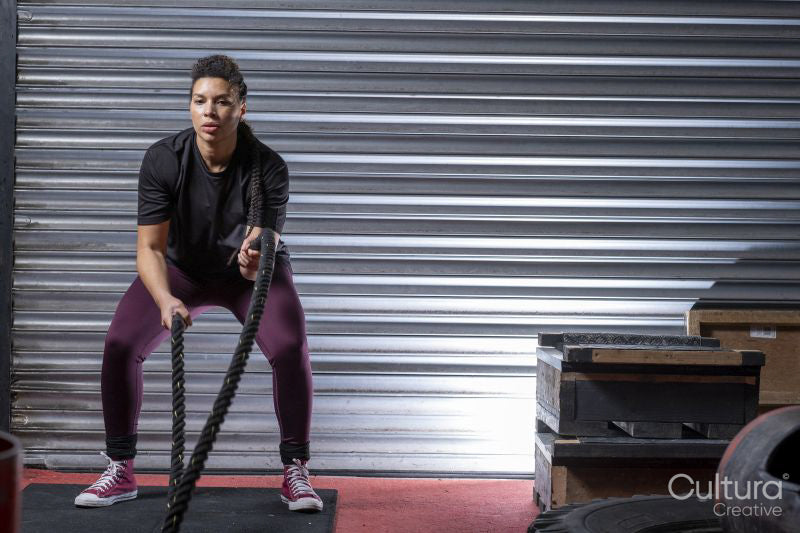 Athletic woman exercising with battle ropes at gym