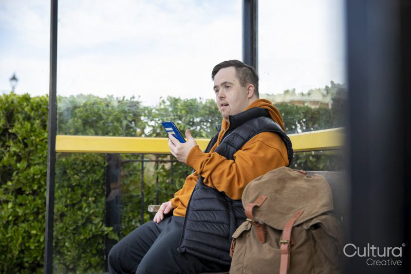 Man sitting on bench at bus stop, using smart phone