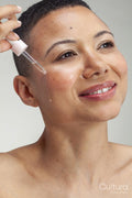 Portrait of smiling woman applying serum on cheek