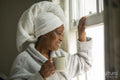 Smiling woman in bathrobe and towel on head looking through window