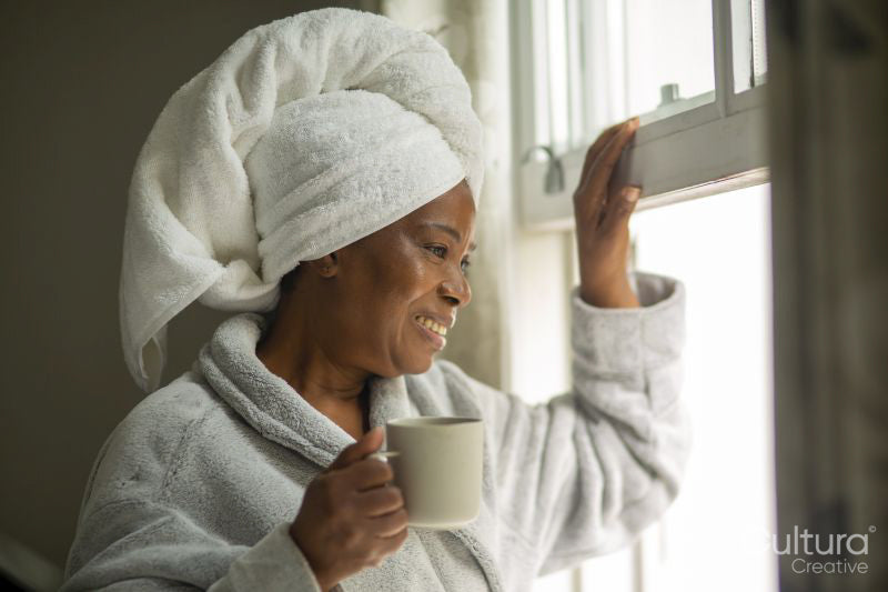 Smiling woman in bathrobe and towel on head looking through window