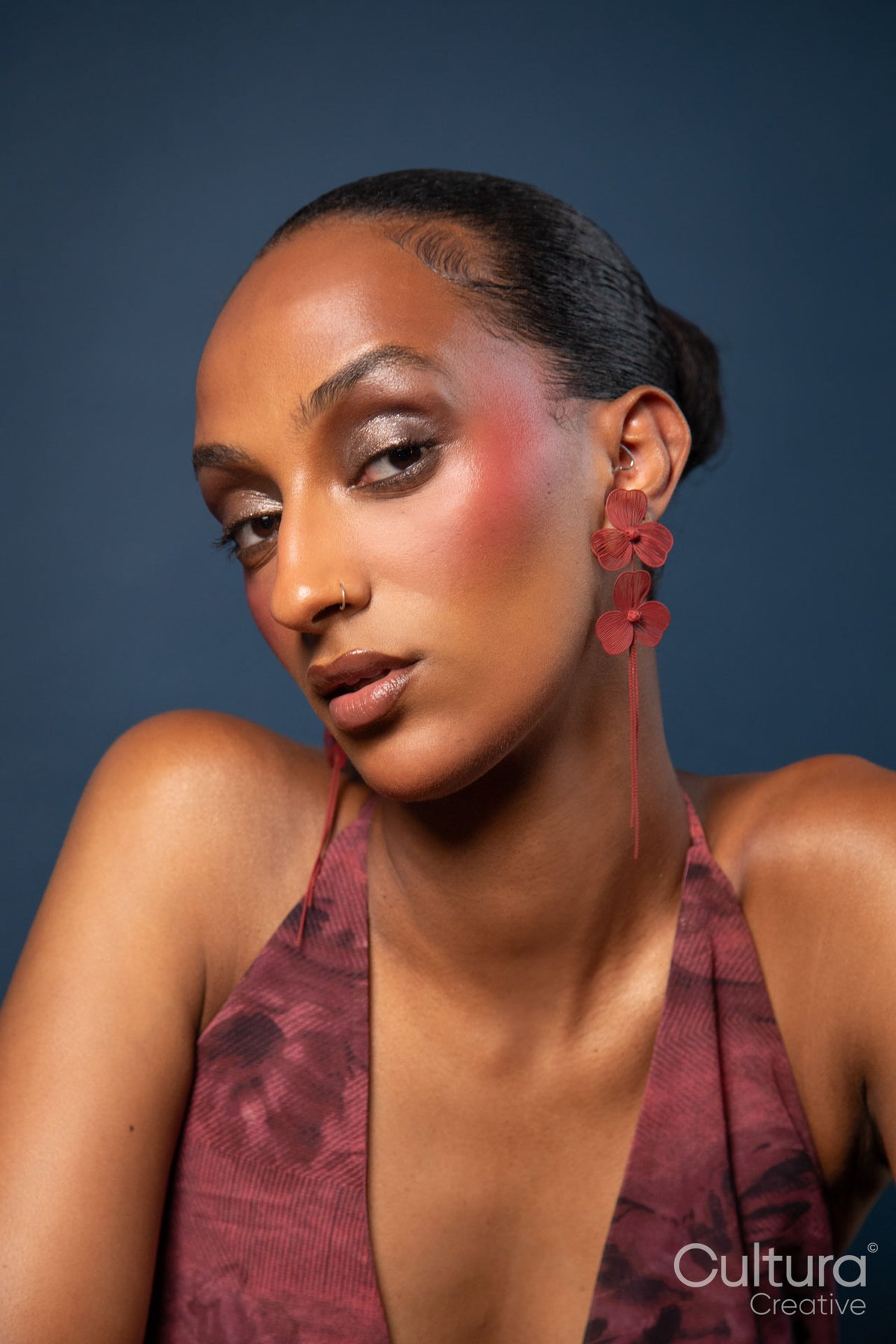 Woman in a burgundy dress and red earrings on a blue background