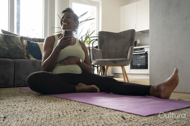 Smiling pregnant woman sitting on yoga mat with smart phone