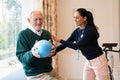 Smiling female therapist assisting senior man exercising with ball