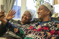 Senior couple sitting on sofa wearing Christmas decorations and waving to phone