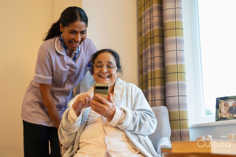 Senior lady looking at phone with nurse in room at nursing home