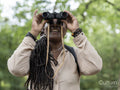 Smiling female hiker looking through binoculars in forest