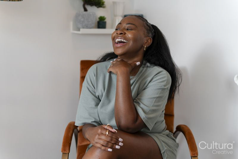 Portrait of young woman laughing while sitting in armchair at home