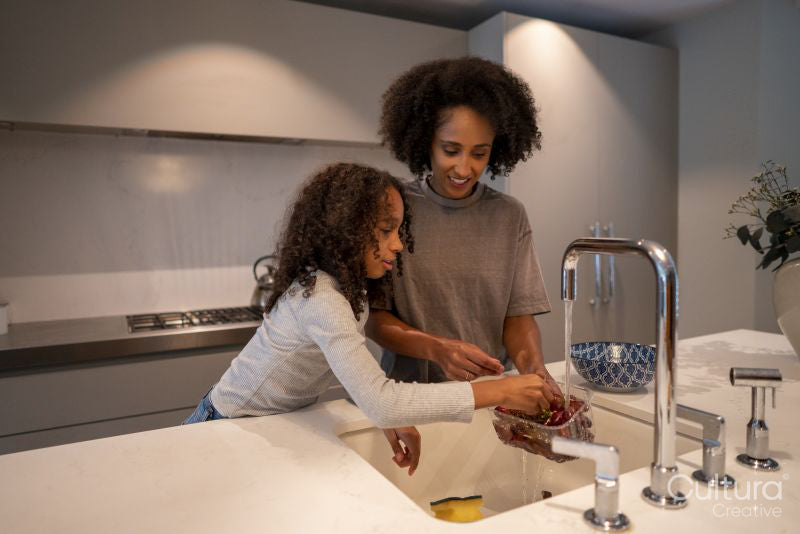 Smiling mother and daughter washing red grapes in kitchen