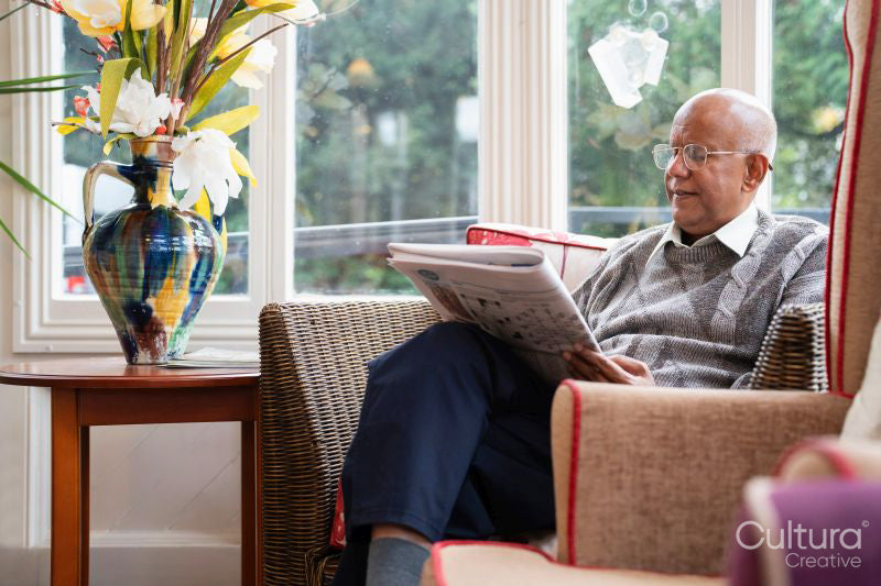 Senior man sitting in armchair and reading newspaper in nursing home