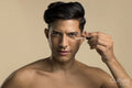 Studio portrait of shirtless man applying foundation under eye