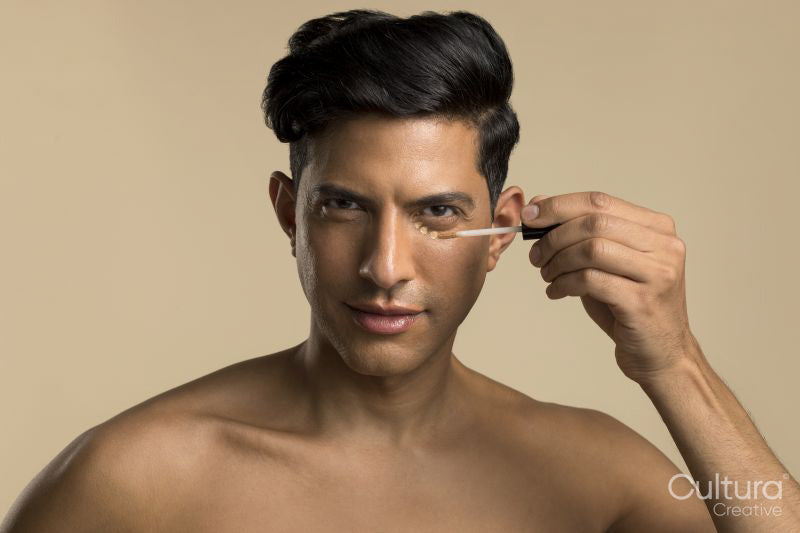 Studio portrait of shirtless man applying foundation under eye