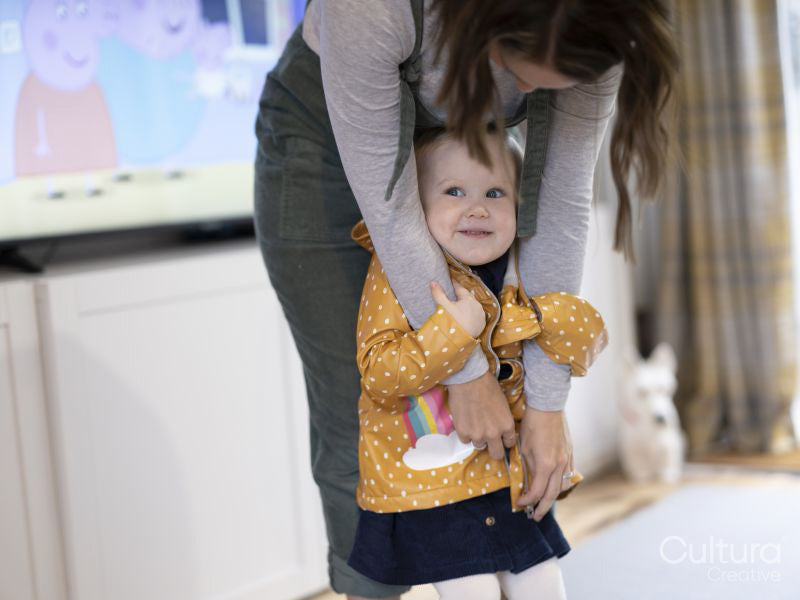 Mother dressing daughter in raincoat