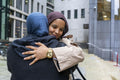 Two women wearing hijabs hugging in street