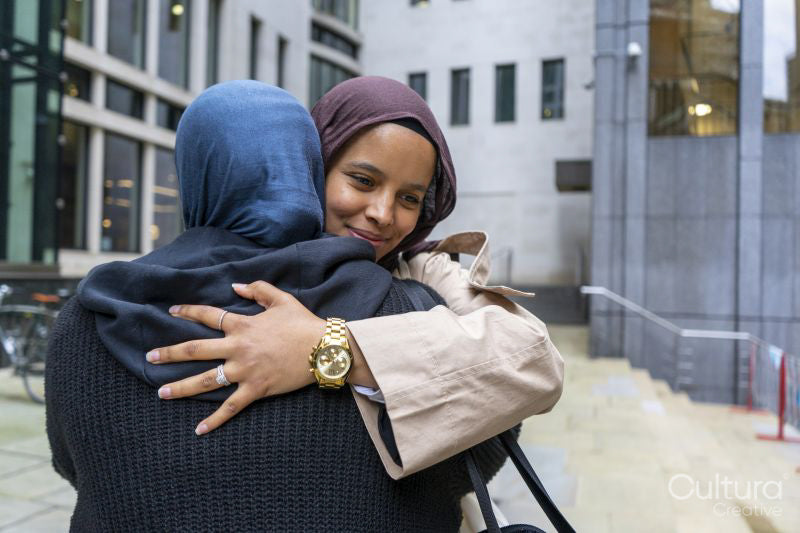 Two women wearing hijabs hugging in street