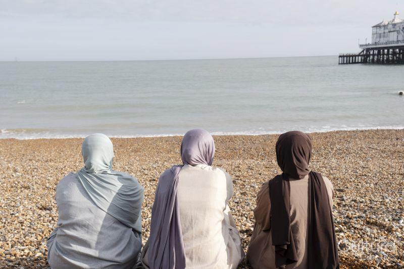 Three Muslim women looking at sea while sitting on beach