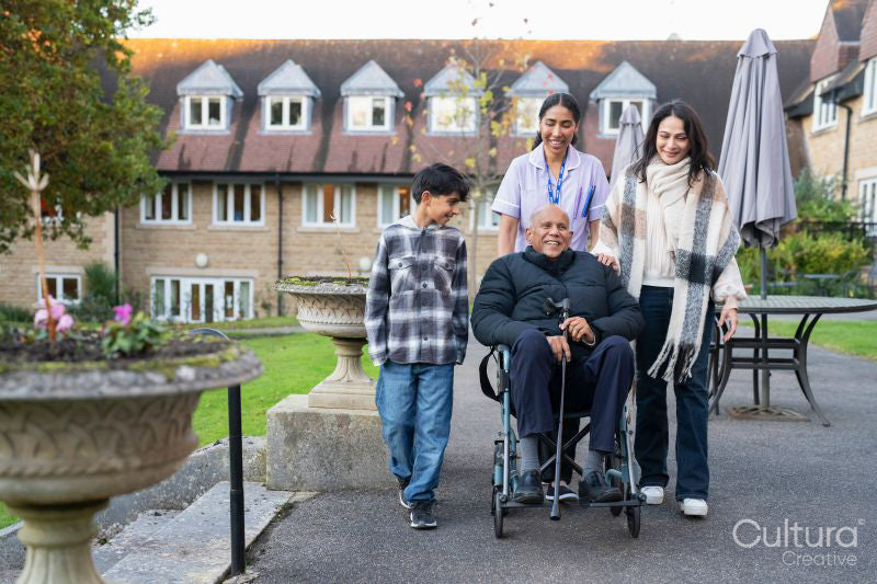 Senior man sitting in wheelchair surrounded by family and care giver outside retirement home