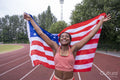 Portrait of smiling athletic woman with American flag on running track