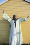 Muslim woman standing with arms outstretched against yellow wall