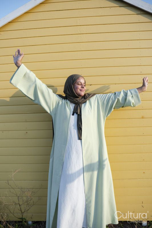 Muslim woman standing with arms outstretched against yellow wall