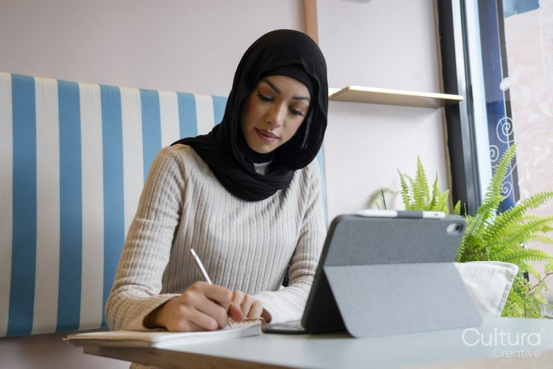 Young woman in hijab working on tablet in cafe