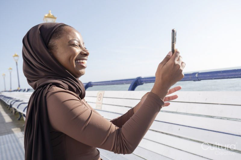 Muslim woman photographing view with smart phone on sunny day