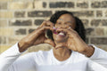 Woman making heart shape with hands against brick wall