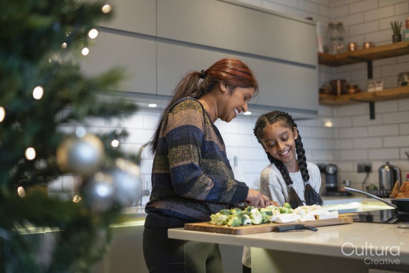 Smiling mother and daughter cutting vegetables in kitchen