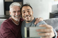 Smiling male couple taking selfie on sofa