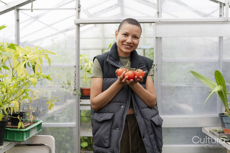 Portrait of smiling woman holding tomatoes in greenhouse