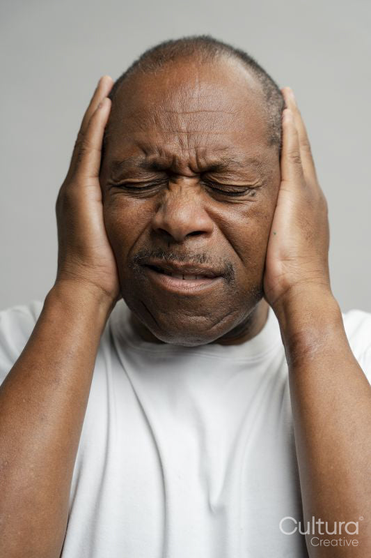 Portrait of man covering ears with hands against gray background