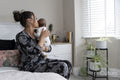Mother carrying newborn baby girl while sitting on bed at home